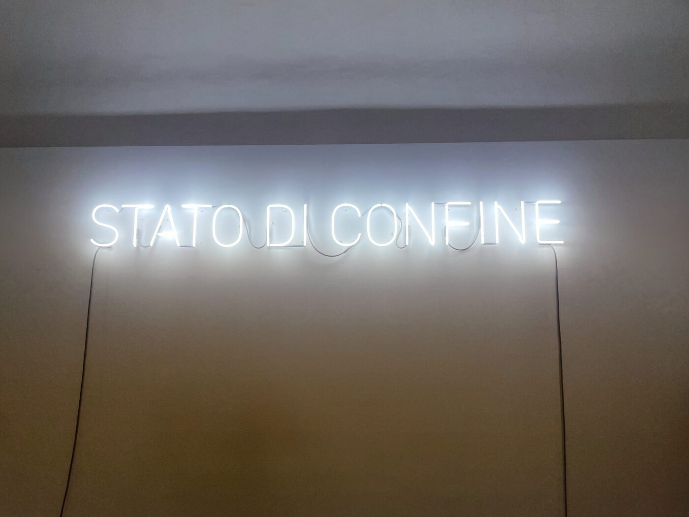 White neon lettering on a gallery wall reading STATO DI CONFINE