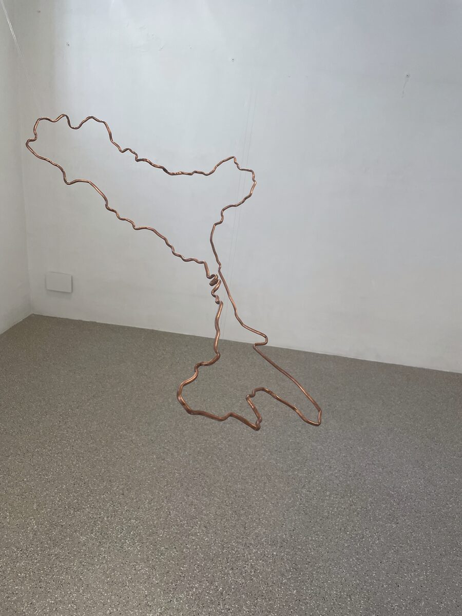 A twisted copper wire hanging on the wall traces the outline of Italy in mid-air